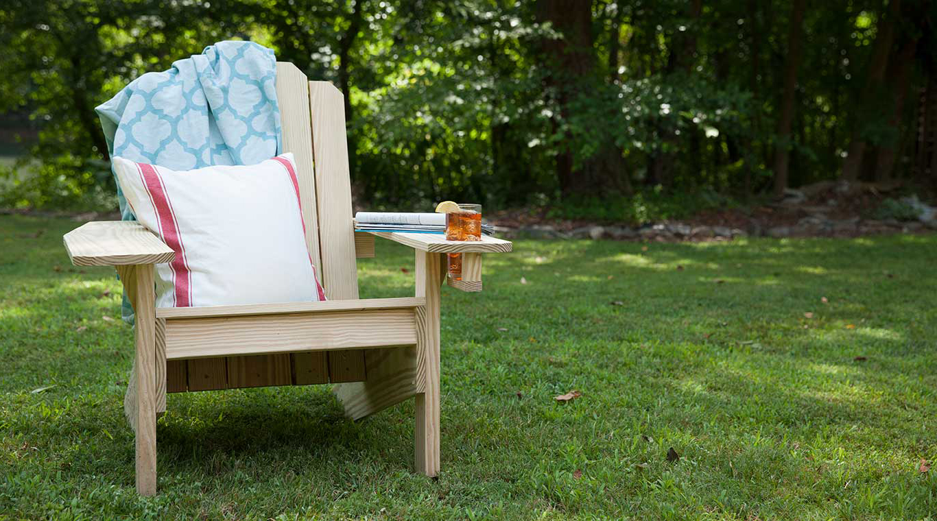 Displays an adirondack chair on green grass with ice tea in the cupholder.